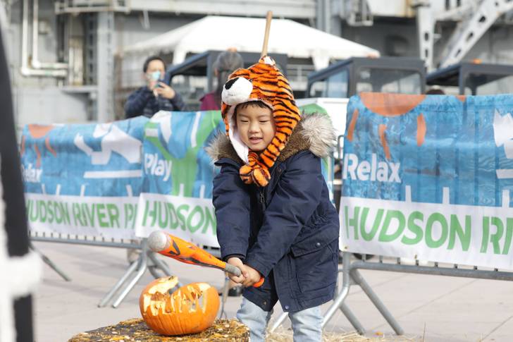 A young child smashes a pumpkin with a bat